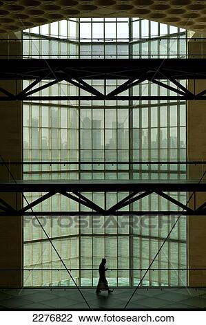 Stock Image - Silhouette of a man in front of large window in the Museum of Islamic Art to the modern city skyline of Doha; Doha, Qatar. Fotosearch
