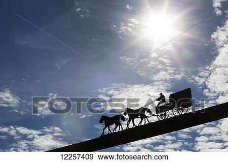 Silhouette of a metal chuckwagon sculpture on a wooden beam with a sun burst and blue sky and clouds; Alberta, Canada View Large Photo Image Stock Photo - Silhouette of a metal chuckwagon sculpture on a wooden beam with a sun burst and blue sky and clouds; Alberta, Canada. Fotosearch