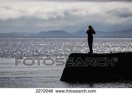 Stock Photo - Silhouette Of A Person Taking A Picture Of The Coastline; Moray Firth Scotland. Fotosearch