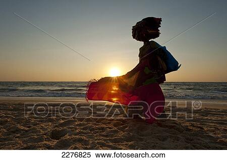Stock Photography - Silhouette of a woman selling Indian cloth on the beach at dusk; Candolim, Goa, India. Fotosearch