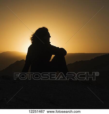 Stock Photo - Silhouette of a woman sitting with a view of the hilly landscape of Valle de la Luna at sunset; San Pedro de Atacama, Antofagasta Region, Chile. Fotosearch