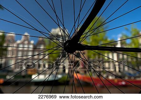 Stock Photo - Silhouette of bicycle wheel in front of canal and traditional gabled houses; Amsterdam, Holland. Fotosearch