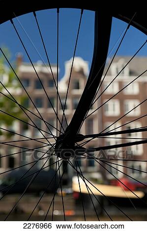 Stock Photograph - Silhouette of bicycle wheel in front of canal and traditional gabled houses; Amsterdam, Holland. Fotosearch