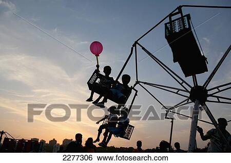 Silhouette of child with balloon and children on fair ground ride at sunset at Chowpatty Beach, new development on Malabar Hill in the background; Mumbai, Maharashtra State, India View Large Photo Image Stock Photograph - Silhouette of child with balloon and children on fair ground ride at sunset at Chowpatty Beach, new development on Malabar Hill in the background; Mumbai, Maharashtra State, India. Fotosearch