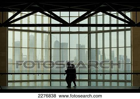 Stock Photo - Silhouette of couple walking past large window in the Museum of Islamic Art in front of the modern city skyline of Doha; Doha, Qatar. Fotosearch