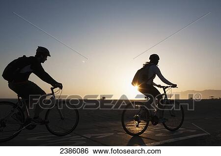 Silhouette of cyclists riding on the promenade beside the beach at sunset; California, United States of America View Large Photo Image Stock Photograph - Silhouette of cyclists riding on the promenade beside the beach at sunset; California, United States of America. Fotosearch
