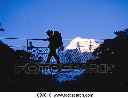 Stock Photograph - Silhouette Of Female Hiker Going Across Suspension Bridge. Fotosearch