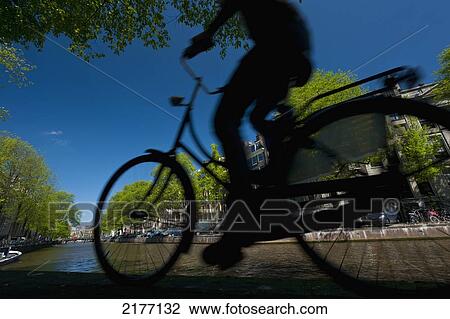 Stock Image - Silhouette Of Man Cycling Past Canal, Amsterdam, Holland.. Fotosearch