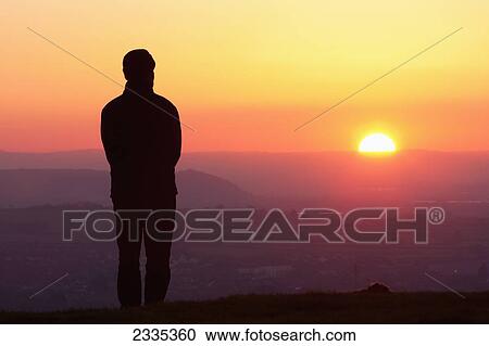 Stock Image - Silhouette Of Man Standing On Glastonbury Tor At Sunset; Glastonbury, Somerset, England, Uk. Fotosearch
