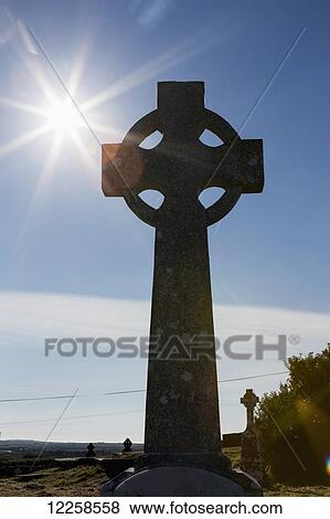 Stock Photo - Silhouette of old celtic cross with sun burst, blue sky and clouds; Carrigaholt, County Clare, Ireland. Fotosearch