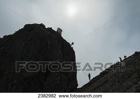 Stock Image - Silhouette of people abseilling off the Inaccessible Pinnacle at the summit of Sgurr Dearg; Isle of Skye, Scotland. Fotosearch