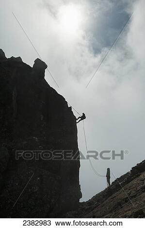 Stock Image - Silhouette of people abseilling off the Inaccessible Pinnacle at the summit of Sgurr Dearg; Isle of Skye, Scotland. Fotosearch