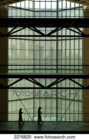 Stock Image - Silhouette of people in front of large window in the Museum of Islamic Art to the modern city skyline of Doha; Doha, Qatar. Fotosearch