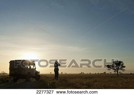 Stock Photo - Silhouette of woman looking through binoculars in front of Mt Kenya at dawn, Ol Pejeta Conservancy; Kenya. Fotosearch