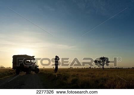 Stock Photograph - Silhouette of woman looking through binoculars in front of Mt Kenya at dawn, Ol Pejeta Conservancy; Kenya. Fotosearch
