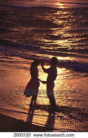 Silhouetted Couple At Sunset Standing In Waters Edge, Golden Reflections View Large Photo Image Stock Image - Silhouetted Couple At Sunset Standing In Waters Edge, Golden Reflections. Fotosearch