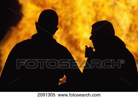 Silhouettes Of Two People, One With Hipflask, In Front Of Large Bonfire At The Ewhurst And Staplecross Bonfire Night, East Sussex, Uk View Large Photo Image Stock Photography - Silhouettes Of Two People, One With Hipflask, In Front Of Large Bonfire At The Ewhurst And Staplecross Bonfire Night, East Sussex, Uk. Fotosearch
