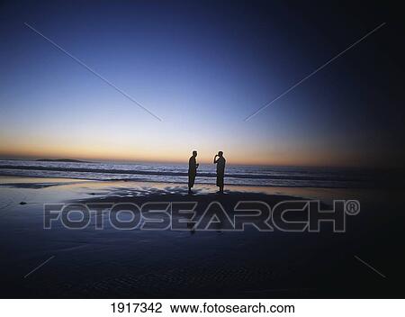 Silhouettes Of Two People Standing On Beach At Dusk View Large Photo Image Stock Image - Silhouettes Of Two People Standing On Beach At Dusk. Fotosearch