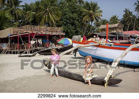 Picture - Silvie Reynolds 6 years old and Isla Reynolds 4 years old stands in front of the many traditional boats and beach front restaurants that line Palolem beach, Goa, India.. Fotosearch