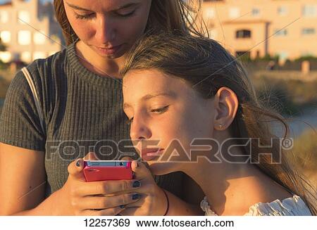 Sisters look at cell phone together; Tarifa, Cadiz, Andalusia, Spain View Large Photo Image Stock Photo - Sisters look at cell phone together; Tarifa, Cadiz, Andalusia, Spain. Fotosearch