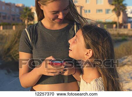 Stock Image - Sisters together with a cell phone; Tarifa, Cadiz, Andalusia, Spain. Fotosearch