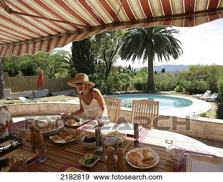 Stock Photo - Sitting at an outdoor table for a meal beside a pool at a villa; France. Fotosearch