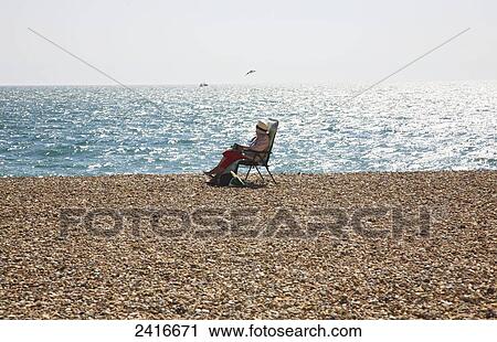 Stock Image - Sitting on a beach chair at the water's edge; Seaford, East Sussex, England. Fotosearch