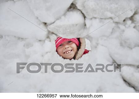 Stock Photo - Six-year-old Caucasian girl peeking through hole in snow fort; Ontario, Canada. Fotosearch