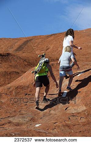 Stock Photo - Skateboarders walking up Uluru, formerly known as Ayers Rock, with their skateboard; Northern Territory, Australia. Fotosearch