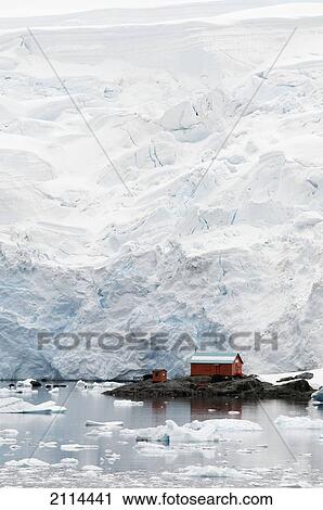 Stock Image - Small Buildings Reflected In The Water On The Frozen Coastline; Antarctica. Fotosearch