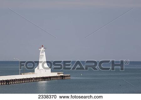 Stock Image - Small White Lighthouse At The End Of A Pier In A Lake With Blue Sky; Burlington, Ontario, Canada. Fotosearch
