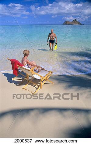 Smiling Senior Man Walks Out Of Turquoise Water, Fins In Hand, Woman Sitting In Lounge Chair View Large Photo Image Stock Photo - Smiling Senior Man Walks Out Of Turquoise Water, Fins In Hand, Woman Sitting In Lounge Chair. Fotosearch