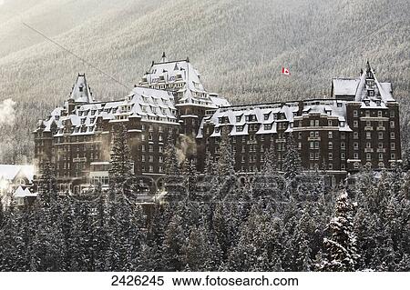 Stock Photography - Snow covered Banff Springs Hotel with snow covered trees and a Canadian flag; Banff, Alberta, Canada. Fotosearch