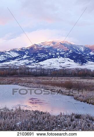 Stock Image - Snow Covered Mountain At Sunset Reflected In Water In Yellowstone National Park; Wyoming United States Of America. Fotosearch