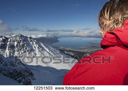 Stock Image - Snowboarder stands looking out at a view of the snow covered mountain landscape; Patagonia, Argentina. Fotosearch