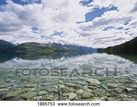 Stock Image - Snowcapped Mountains Reflected In Lake Wakatipu With Clear Water And Pebbles. Fotosearch