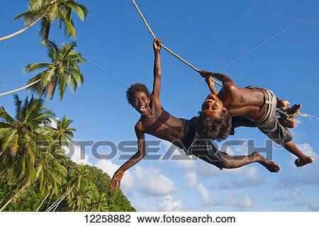 Stock Image - Solomon Island kids swinging from a rope; Gizo, Western Province, Solomon Islands. Fotosearch