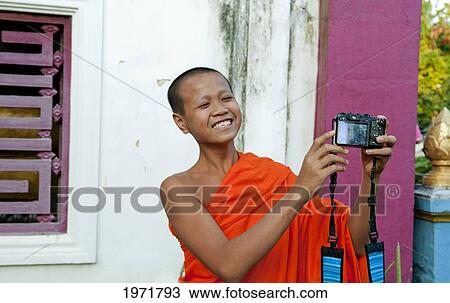 Stock Image - South East Asia, Laos, Luang Prabang, A Young Monk Laughs As He Takes His Own Picture With A Visitor's Camera.. Fotosearch
