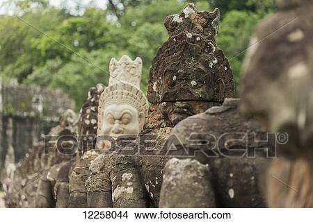 Picture - South gate of Angkor, connecting Bayon Wat and Angkor Wat, in the laterals many buddhas are holding a big snake, the gate is made by a tower with four buddha faces; Siem Reap, Cambodia. Fotosearch