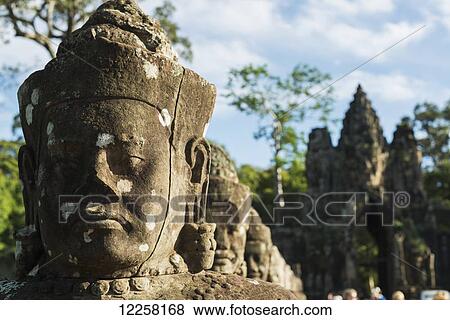 Stock Photo - South gate of Angkor, connecting Bayon Wat and Angkor Wat, in the laterals many buddhas are holding a big snake, the gate is made by a tower with four buddha faces; Siem Reap, Cambodia. Fotosearch