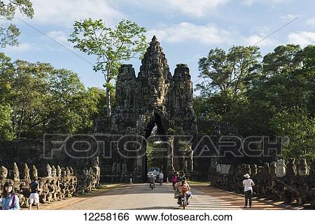 Stock Photograph - South gate of Angkor, connecting Bayon Wat and Angkor Wat, in the laterals many buddhas are holding a big snake, the gate is made by a tower with four buddha faces; Siem Reap, Cambodia. Fotosearch