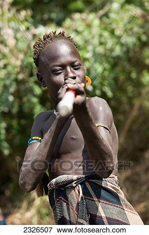 Stock Photo - South Western Ethiopia, Omo Valley, Southern Mursiland, Local Mursi boy playing with surveying ranging pole; Dirikoro. Fotosearch