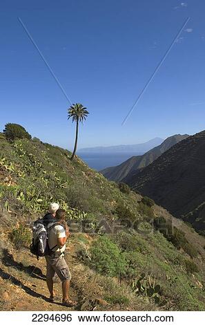 Stock Photograph - Spain, Canary Islands, Tourist hiking near on Vallehermoso trail with Island of Tenerife in background; Island of La Gomera. Fotosearch