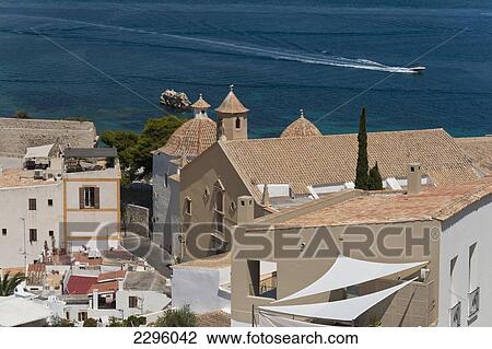 Stock Image - Spain, Ibiza, Looking over shaded roof terrace and Santo Domingo church in Dalt Vila; Ibiza Town. Fotosearch