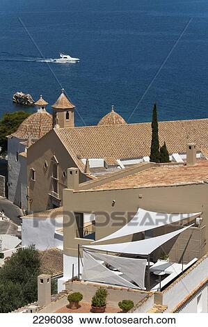 Stock Photo - Spain, Ibiza, Looking over shaded roof terrace and Santo Domingo church in Dalt Vila; Ibiza Town. Fotosearch