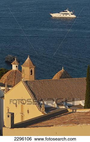 Stock Photograph - Spain, Ibiza, Looking over shaded roof terrace and Santo Domingo church in Dalt Vila; Ibiza Town. Fotosearch