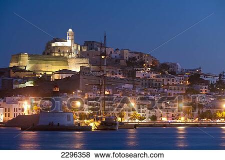 Stock Photo - Spain, Looking across harbor to Ibiza town at dusk; Ibiza. Fotosearch