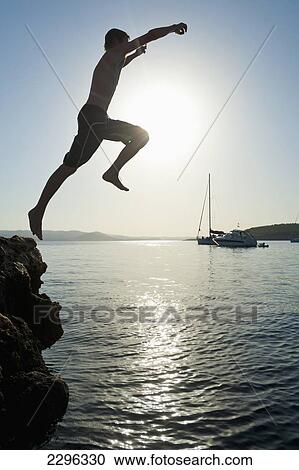 Stock Image - Spain, Man jumping off rocks into sea beside La Basse beach; Ibiza. Fotosearch