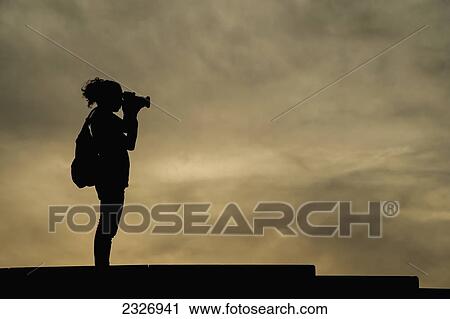 Stock Image - Spain, Parc del Forum; Barcelona, Primavera Sound music festival, Girl taking a photograph at dusk. Fotosearch
