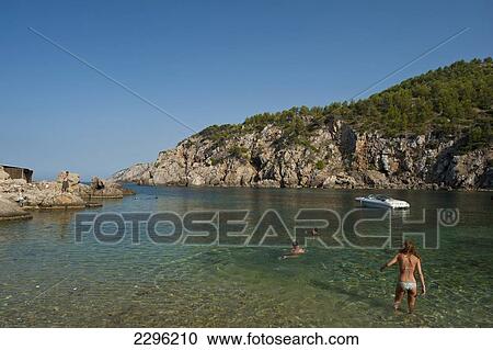 Stock Image - Spain, People going to swim off Cala d'en Serra beach; Ibiza. Fotosearch